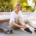 Upset skater girl holding her painful leg with skateboard