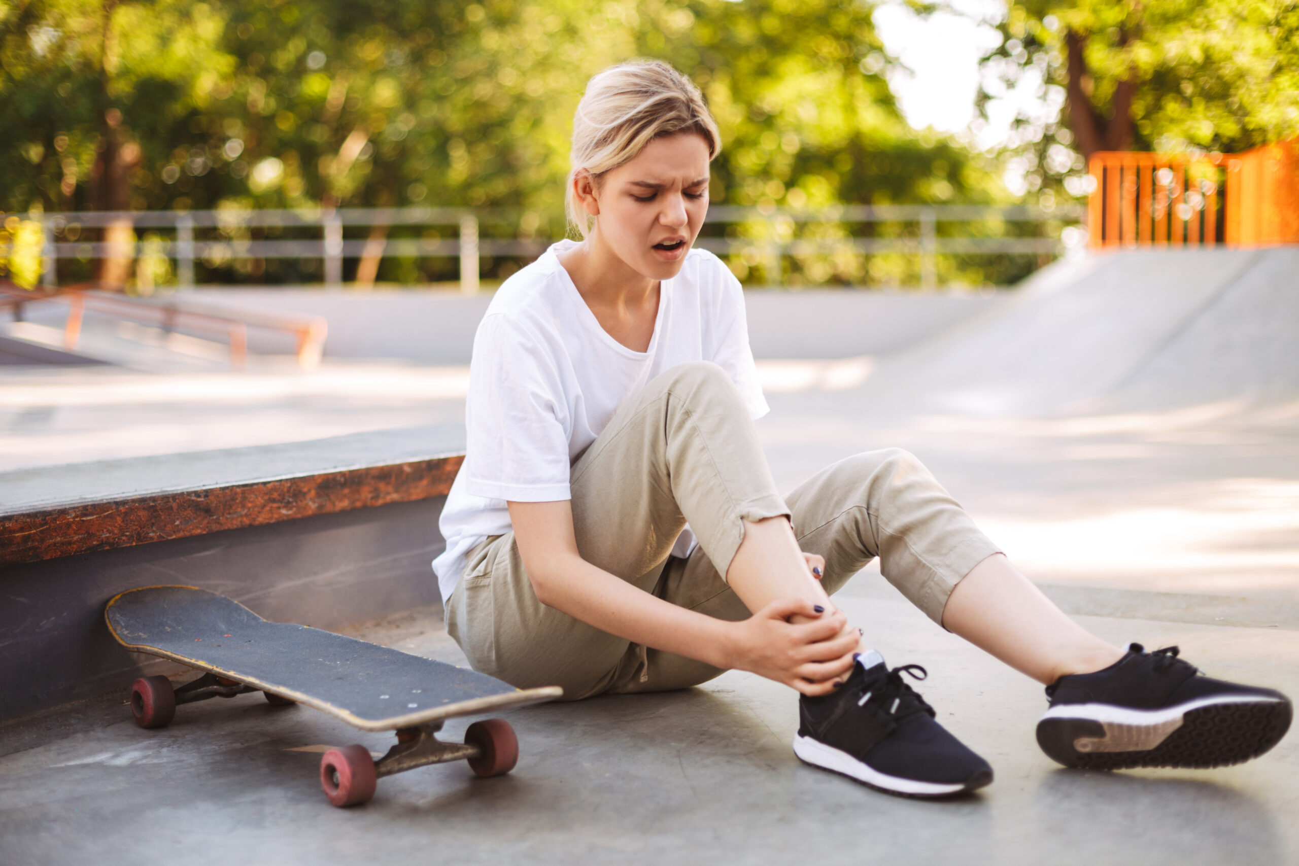 Upset skater girl holding her painful leg with skateboard